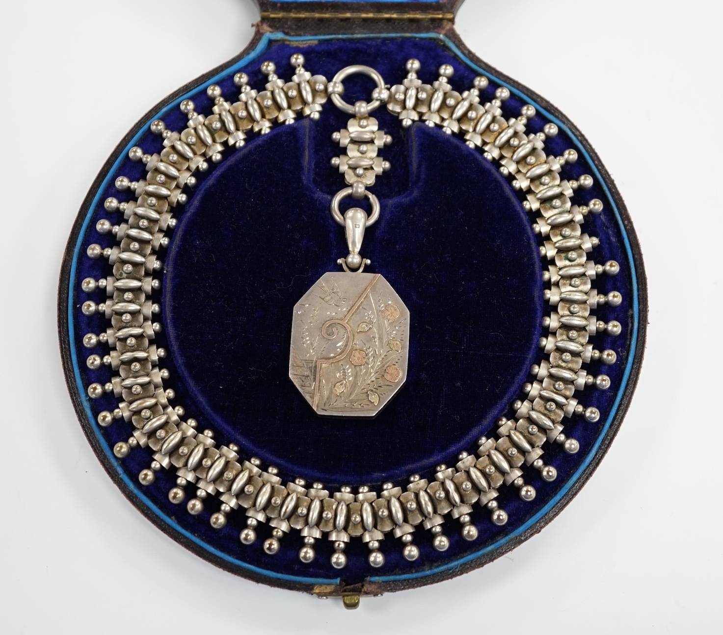 A Victorian silver octagonal locket with engraved aesthetic decoration, Birmingham, 1881, 43mm, on a white metal Etruscan revival chain, 42cm, in fitted case.